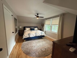 Un dormitorio con cama, ventilador de techo, ventana con persianas, mesita de noche y cómoda.