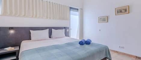 A hotel room with a bed, a bedside table, a window with curtains, and two wall-mounted pictures.