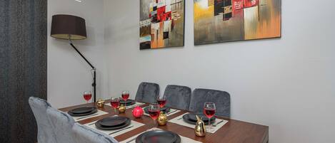 Una sala da pranzo con un tavolo in legno apparecchiato per sei persone, sedie rivestite in grigio e due dipinti astratti appesi al muro.