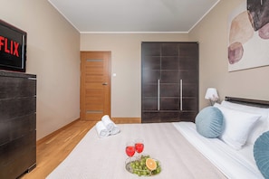 A hotel room with a wooden wardrobe, a bed with blue and white pillows, a bedside table with a lamp, and a wall-mounted TV displaying 'FLIX'. - Lumina Comfort 3-room Apt w/ Parking I Balcony (Warszawa)