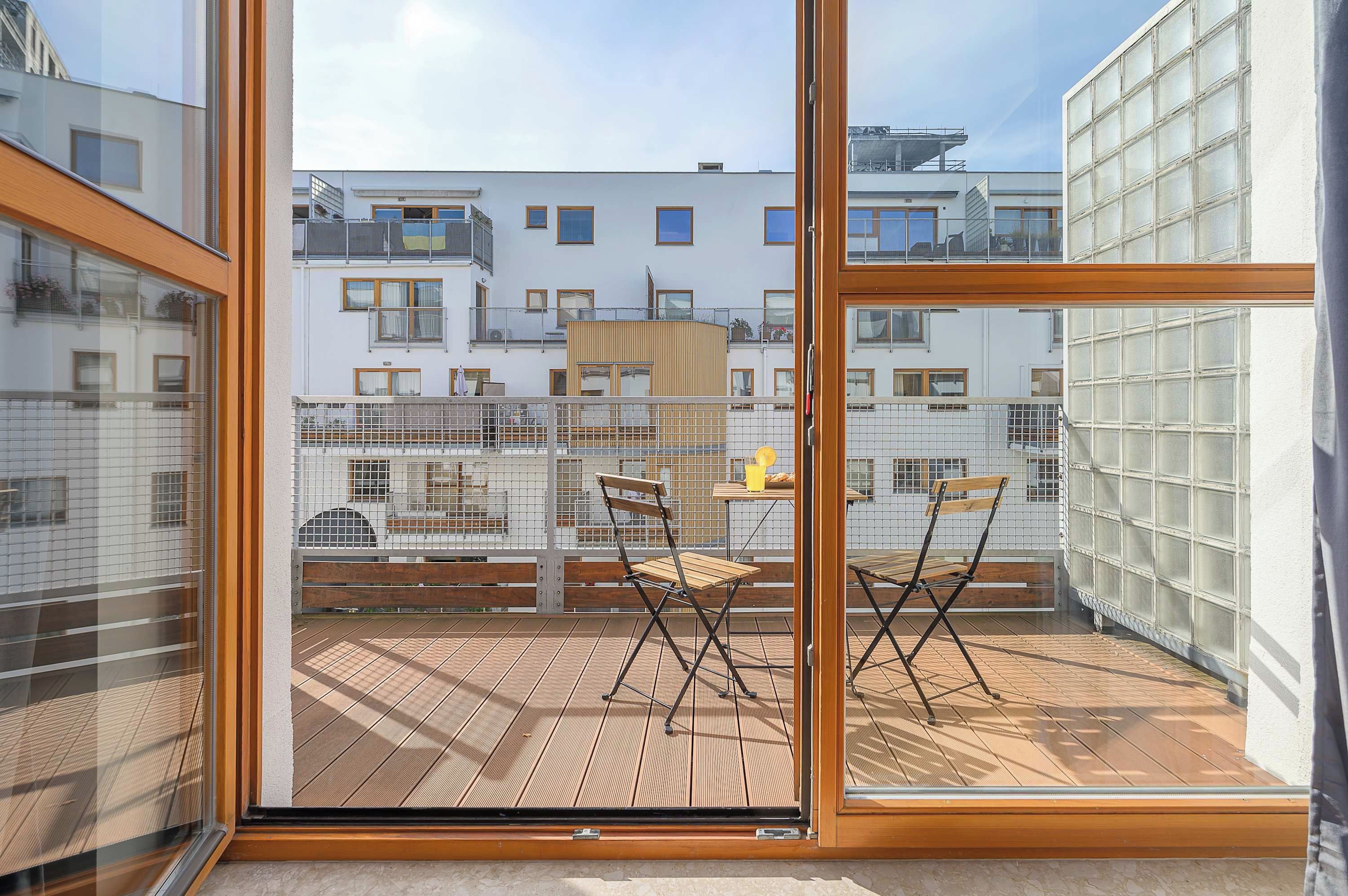 A balcony with two wooden chairs, a table, and a view of neighboring buildings.