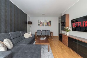 A modern living room with a grey sofa, a coffee table, a dining area with chairs, a TV, and artwork on the wall. - Lumina Comfort 3-room Apt w/ Parking I Balcony (Warszawa)
