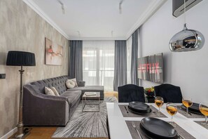 Uma sala de estar moderna com um sofá cinzento, uma mesa de centro e um espaço de jantar com mesa e cadeiras.
