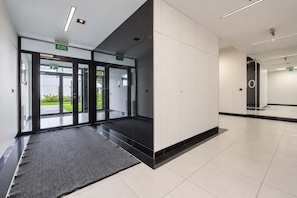 Eine moderne Hotelhalle mit Glastüren, schwarzem Teppich und einem sauberen, gefliesten Boden.