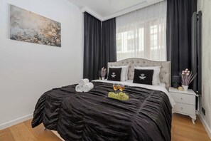 A modern bedroom with a large bed, dark curtains, a painting on the wall, and a bedside table with a plant. - Lumina 3-room Apart w/ Terrace I Parking (Warszawa)