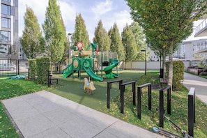 A playground with a slide and climbing structures, surrounded by trees and a paved walkway. - Lumina 3-room Apart w/ Terrace I Parking (Warszawa)
