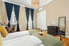 Ein Schlafzimmer mit Bett, Schreibtisch, Stuhl, Kommode, Spiegel und einem Fenster mit Vorhängen.