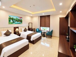A hotel room with two beds, a desk, a chair, a window with blinds, and a painting on the wall. - MAISON PARK (Vo Cuong)