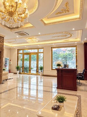 A hotel lobby with a marble floor, a reception desk, a chandelier, and large windows. - MAISON PARK (Vo Cuong)