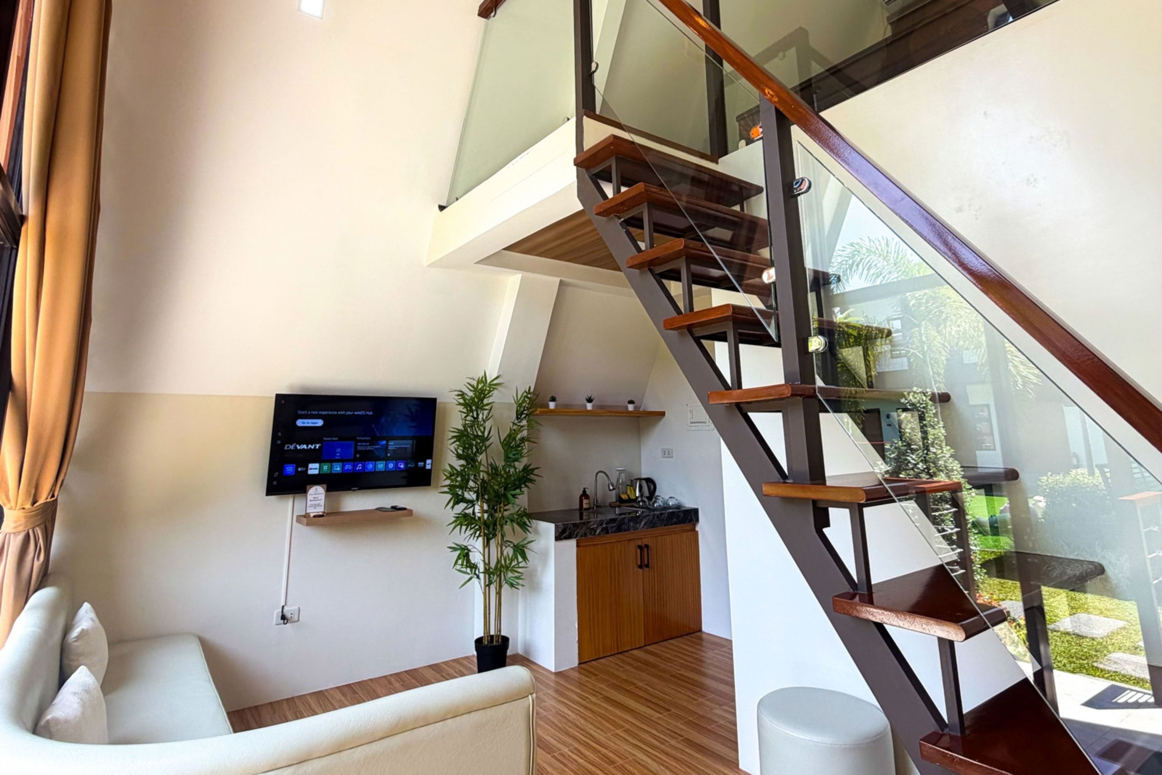 A modern living space with a staircase, a flat-screen TV, a sofa, and a kitchen area.