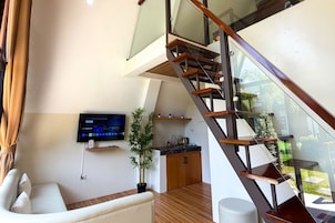 A modern living space with a staircase, a flat-screen TV, a sofa, and a kitchen area.