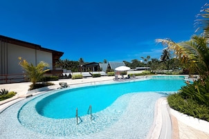 A swimming pool with a curved edge, surrounded by palm trees and a building with a flat roof.