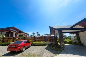 A red car parked in front of a modern building with a covered entrance and a stone wall. - Eddielita Resort San Juan Batangas (San Juan)