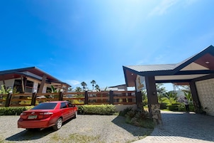 A red car parked in front of a modern building with a covered entrance and a stone wall.