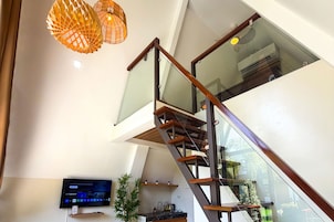 Un interior moderno con una escalera de cristal, un televisor de pantalla plana y una planta de bambú.