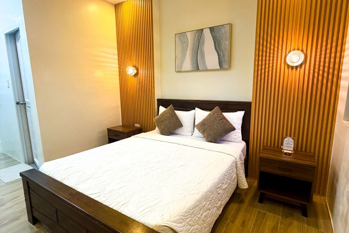 Een hotelkamer met een groot bed, een houten hoofdbord, twee nachtkastjes, een wandlamp en een schilderij boven het bed.
