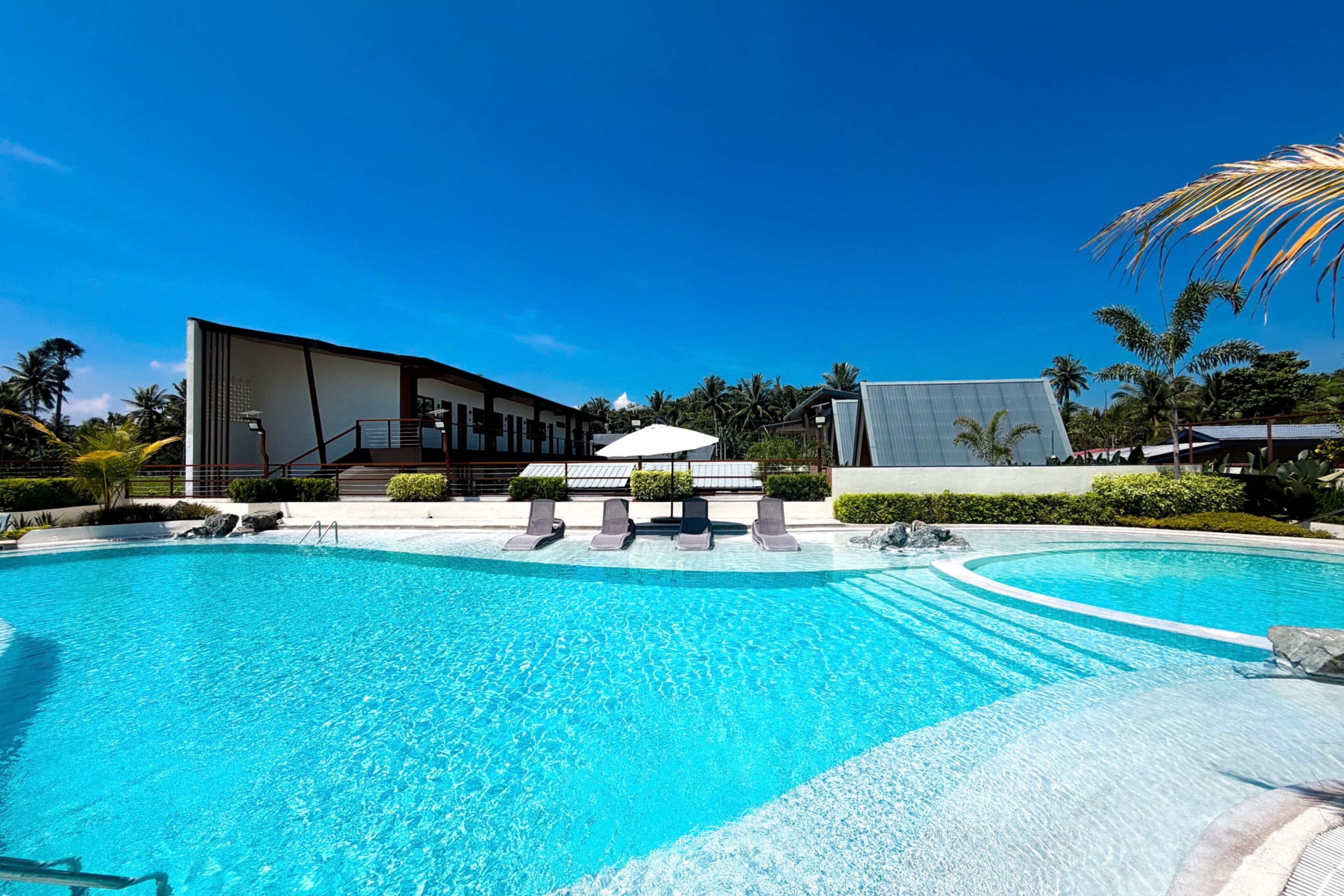 Una piscina con sillones de descanso y un edificio de diseño moderno.