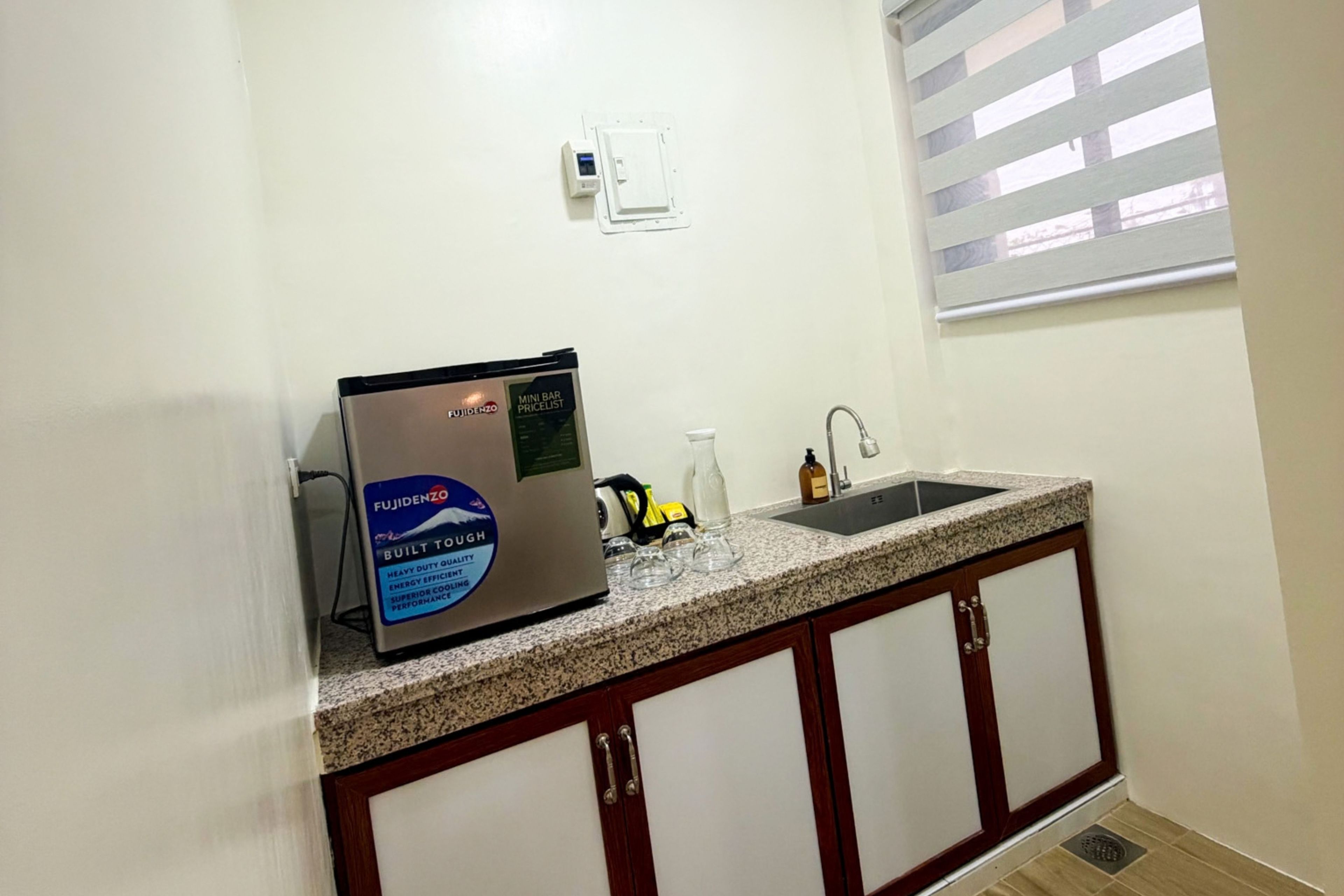 A kitchen with a built-in mini fridge, a sink, and a window with blinds.