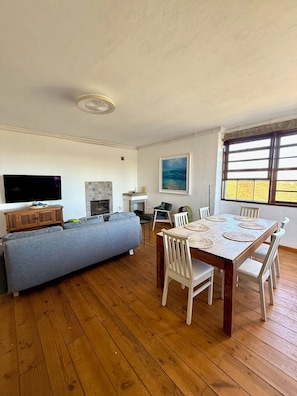 A living room with a sofa, TV, fireplace, dining table with chairs, and a painting. - Secluded Mountainside Retreat w/ Pool, Sauna + Gym (Caldas de Monchique)