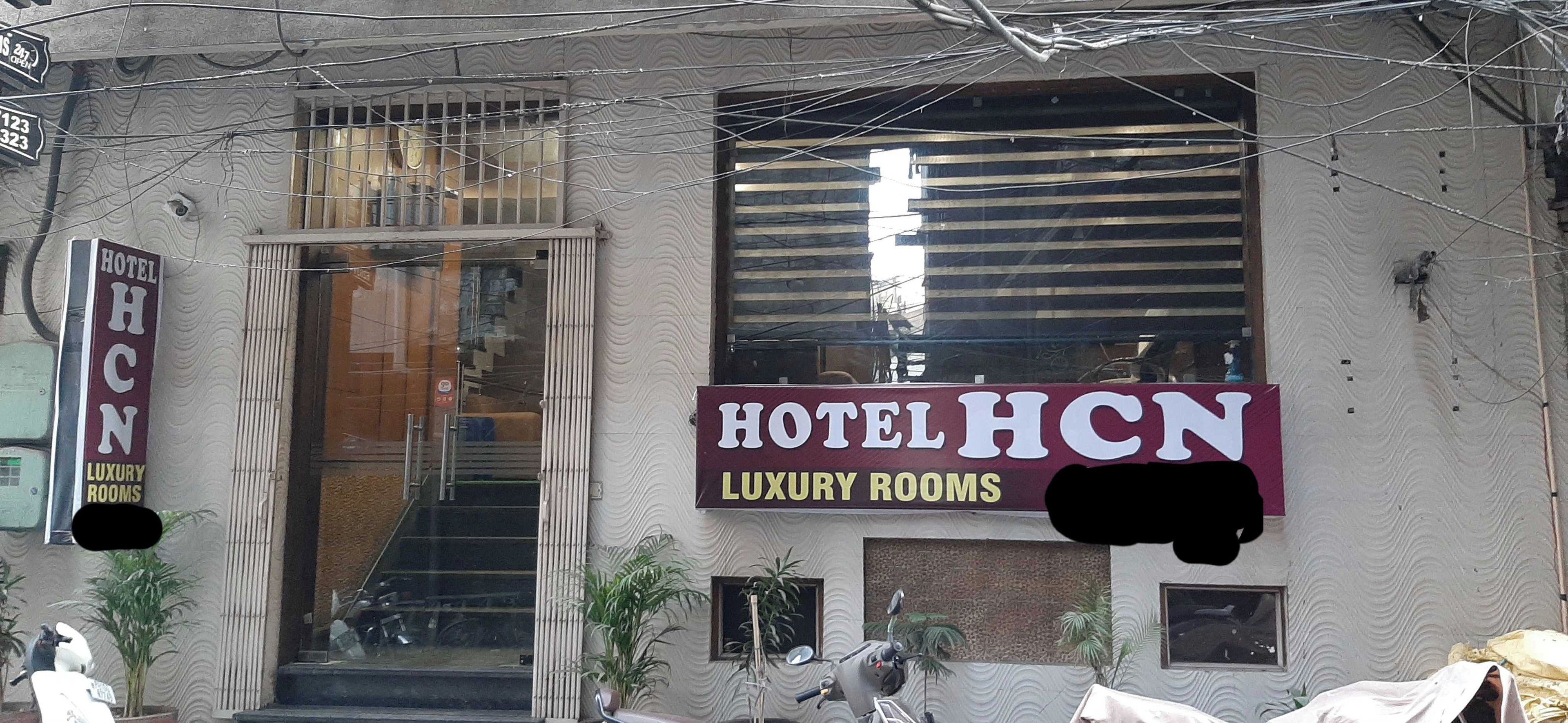 A building with a sign for 'HOTEL HCN LUXURY ROOMS' and a visible entrance with steps leading up to the door.
