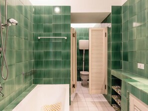 Ein Badezimmer mit grünen Fliesen, einer Badewanne, einer Toilette und einer Dusche.