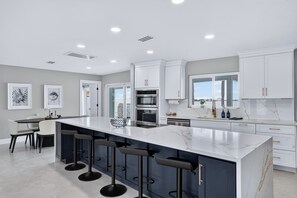 A modern kitchen with a large island, bar stools, and a dining area with chairs. - Waterfront Getaway Pool, Boat Dock & Kayaks (St. Petersburg)