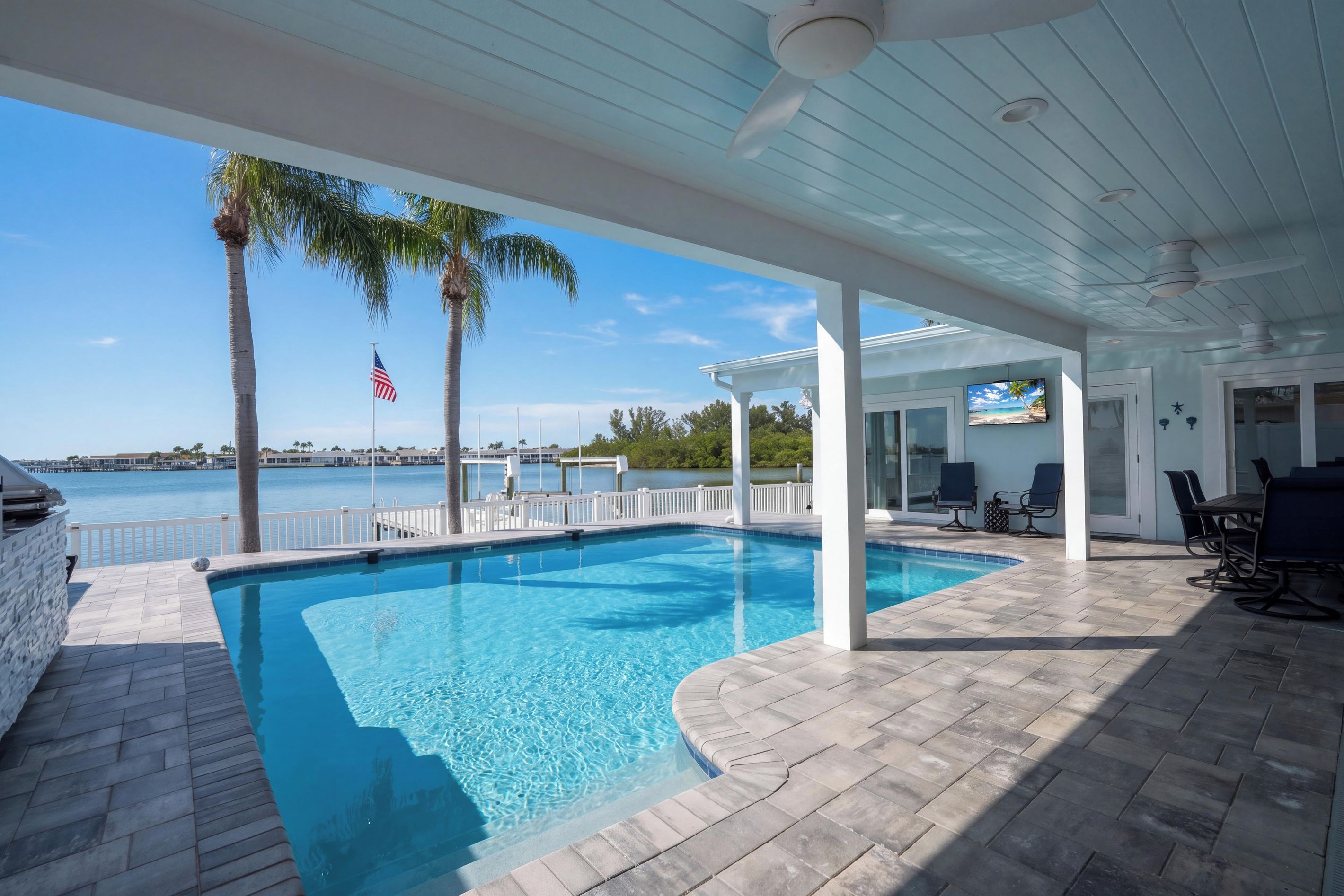 A swimming pool with a view of the water, a covered patio area, and a flag.