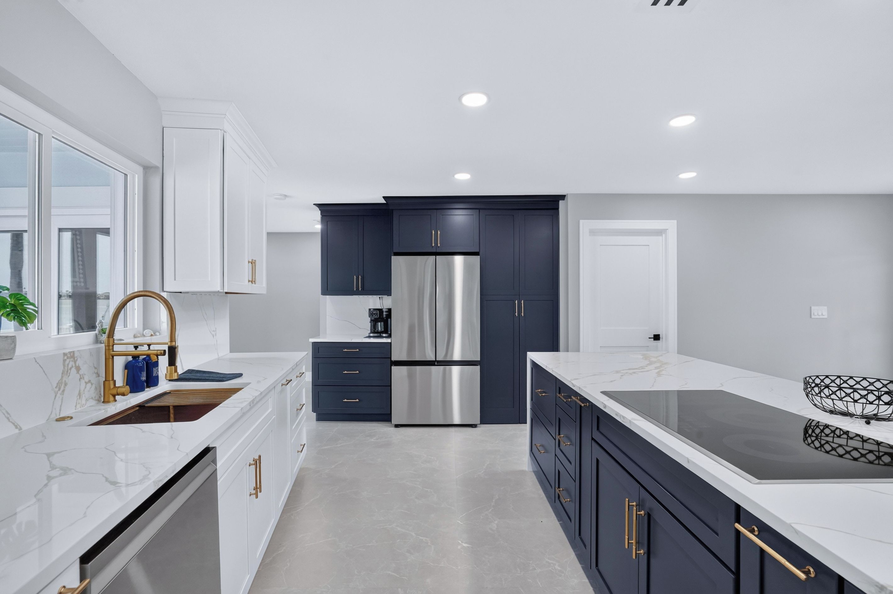 A modern kitchen with white cabinetry, a stainless steel refrigerator, and a marble countertop.