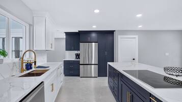 A modern kitchen with white cabinetry, a stainless steel refrigerator, and a marble countertop.