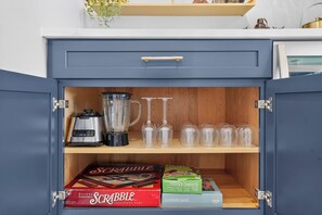 A cabinet with a drawer containing a coffee maker, a blender, wine glasses, and two boxes of Scrabble. - Waterfront Getaway Pool, Boat Dock & Kayaks (St. Petersburg)