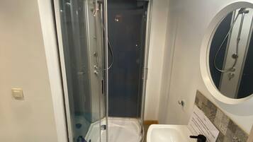 A bathroom with a glass-enclosed shower, a white sink, and a mirror.