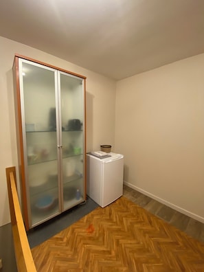 A room with a wooden herringbone floor, a white washing machine, and a glass-fronted wardrobe. - Studio with air conditioning and bike storage (Huy)