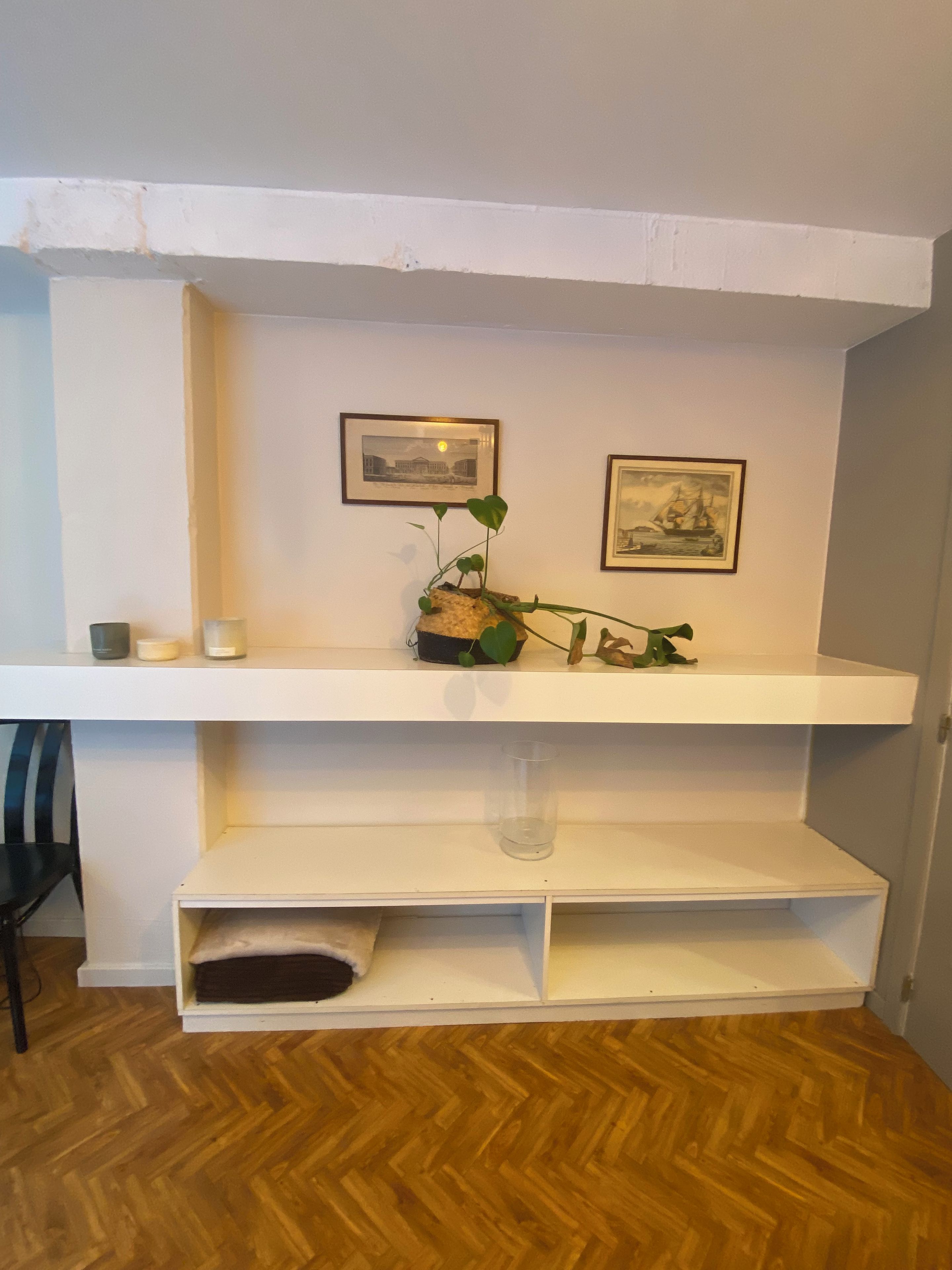 A white shelf with two framed pictures, a potted plant, and a candle.