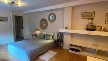 Ein Schlafzimmer mit einem Bett, Nachttischen, einem Sessel, einem Regal mit Dekorationen und einem Fischgrätparkett.