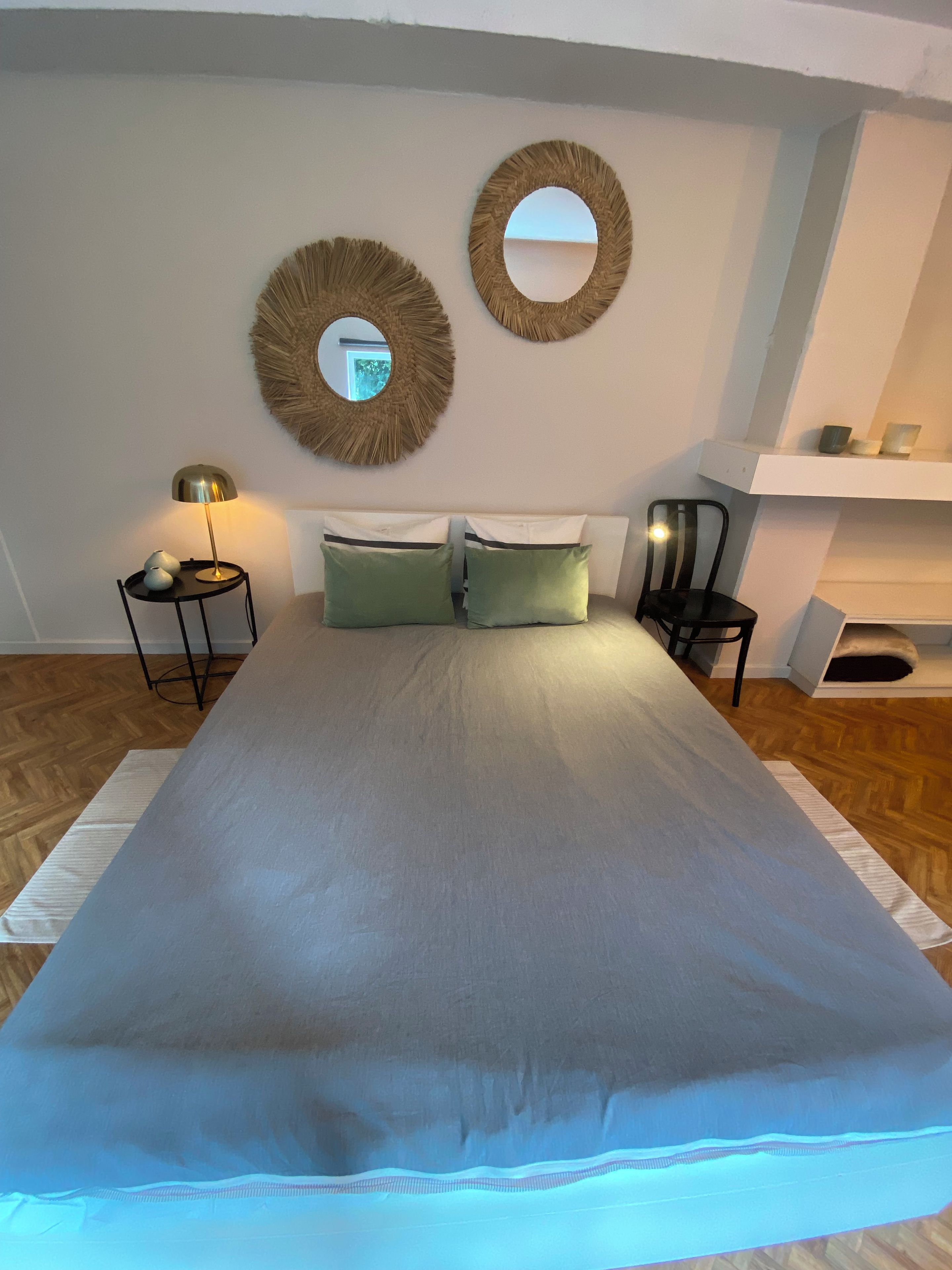 Een slaapkamer met een groot bed, twee spiegelwanden, een bedlampje en een klein nachtkastje.