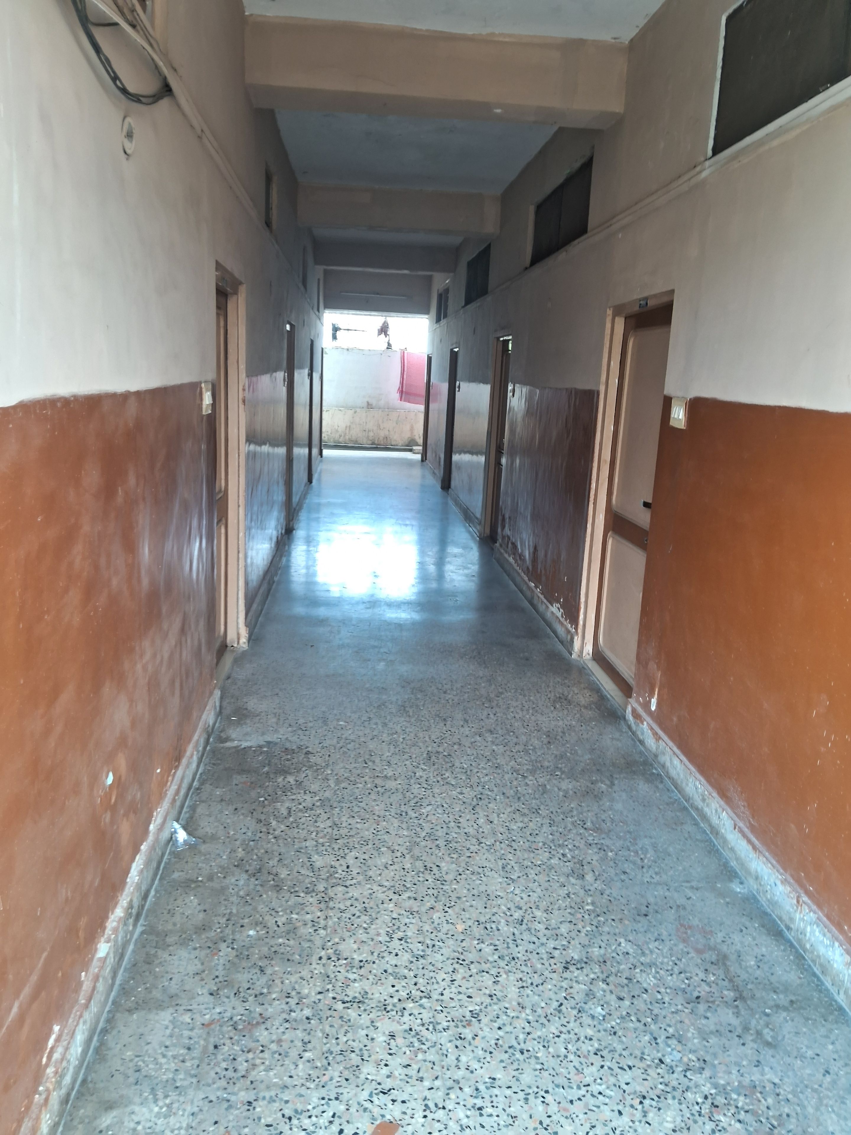 A corridor with doors on both sides, leading to an open area with a view of the outside.