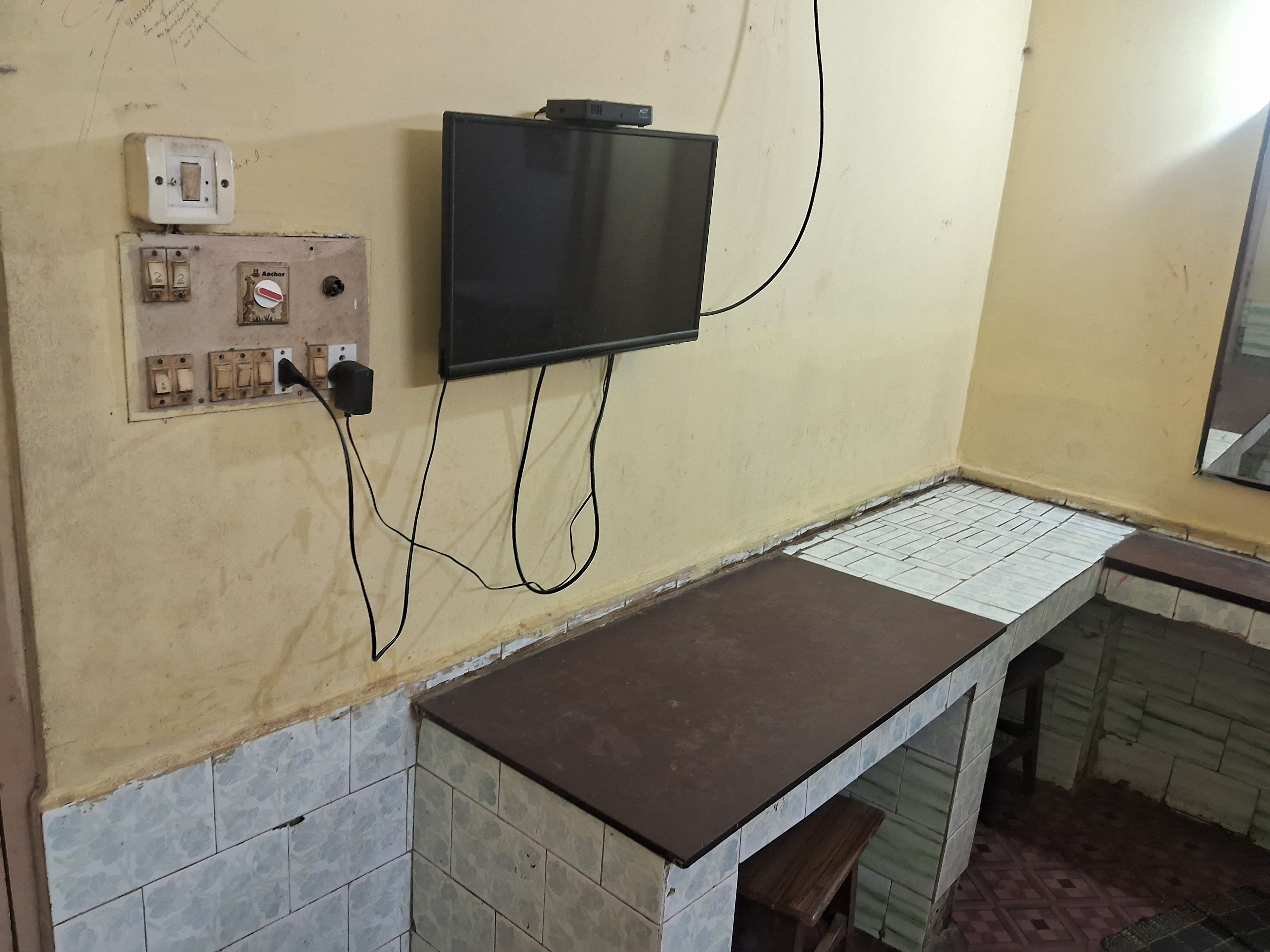 A room with a television mounted on the wall, electrical outlets, and a tiled counter.