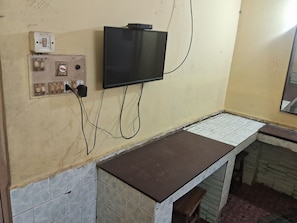 A room with a television mounted on the wall, electrical outlets, and a tiled counter. - Hotel Swamy Lodge  (Vijayawada)