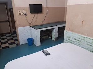 A room with a bed, a desk with a television mounted above it, and a blue bucket on the floor. - Hotel Swamy Lodge  (Vijayawada)