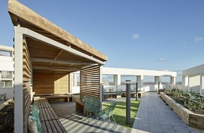 En takterrass med en pergola av trä, en sittgrupp och utsikt över staden.