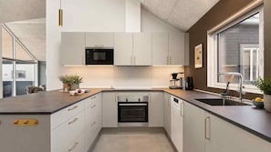 A modern kitchen with white cabinetry, a built-in oven, a microwave, and a large window providing natural light. - VillaVilla 997 - Odsherred, Nordsjælland (Højby)