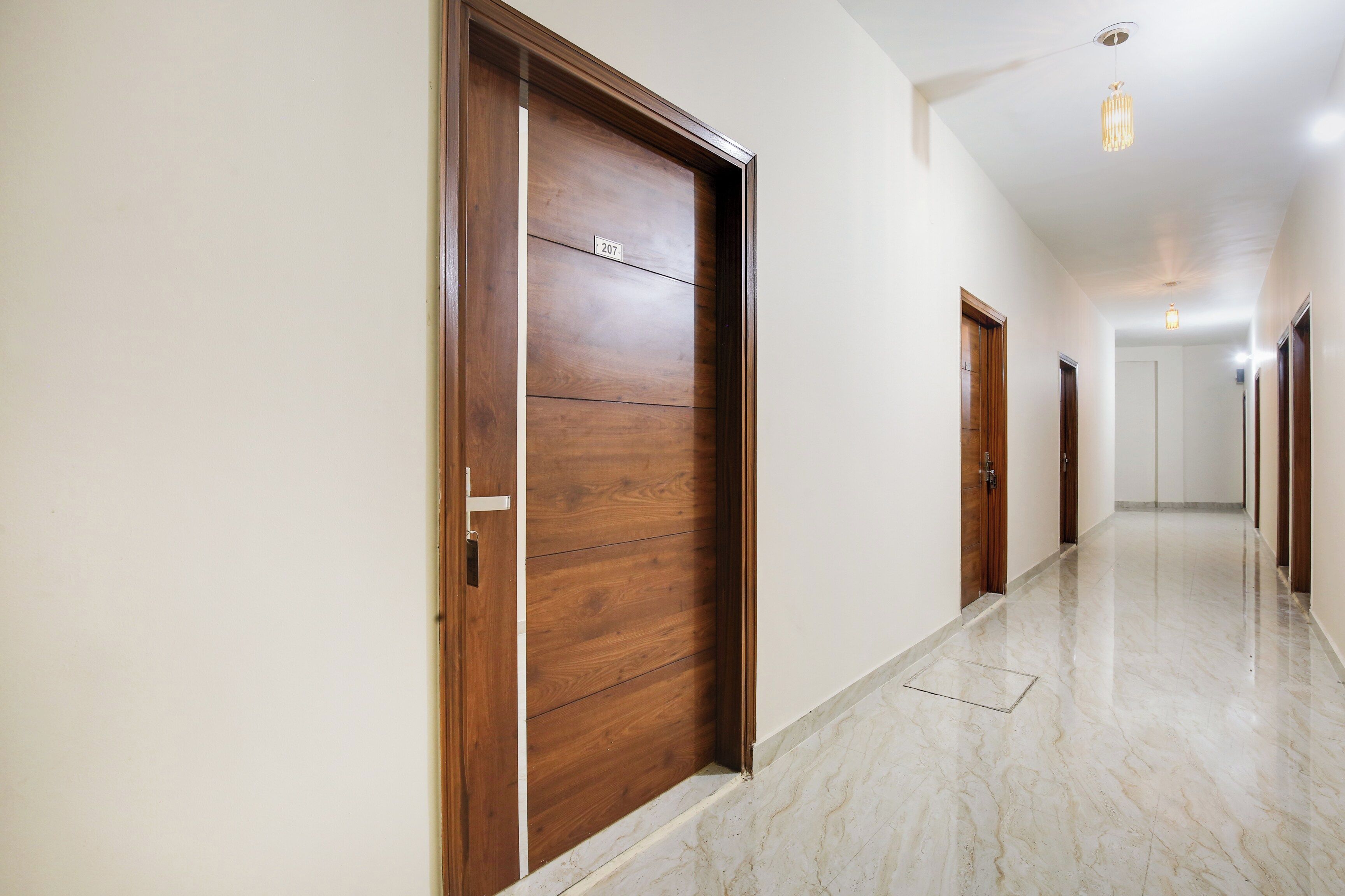 Corredor com portas de madeira, piso de mármore e luminária no teto.