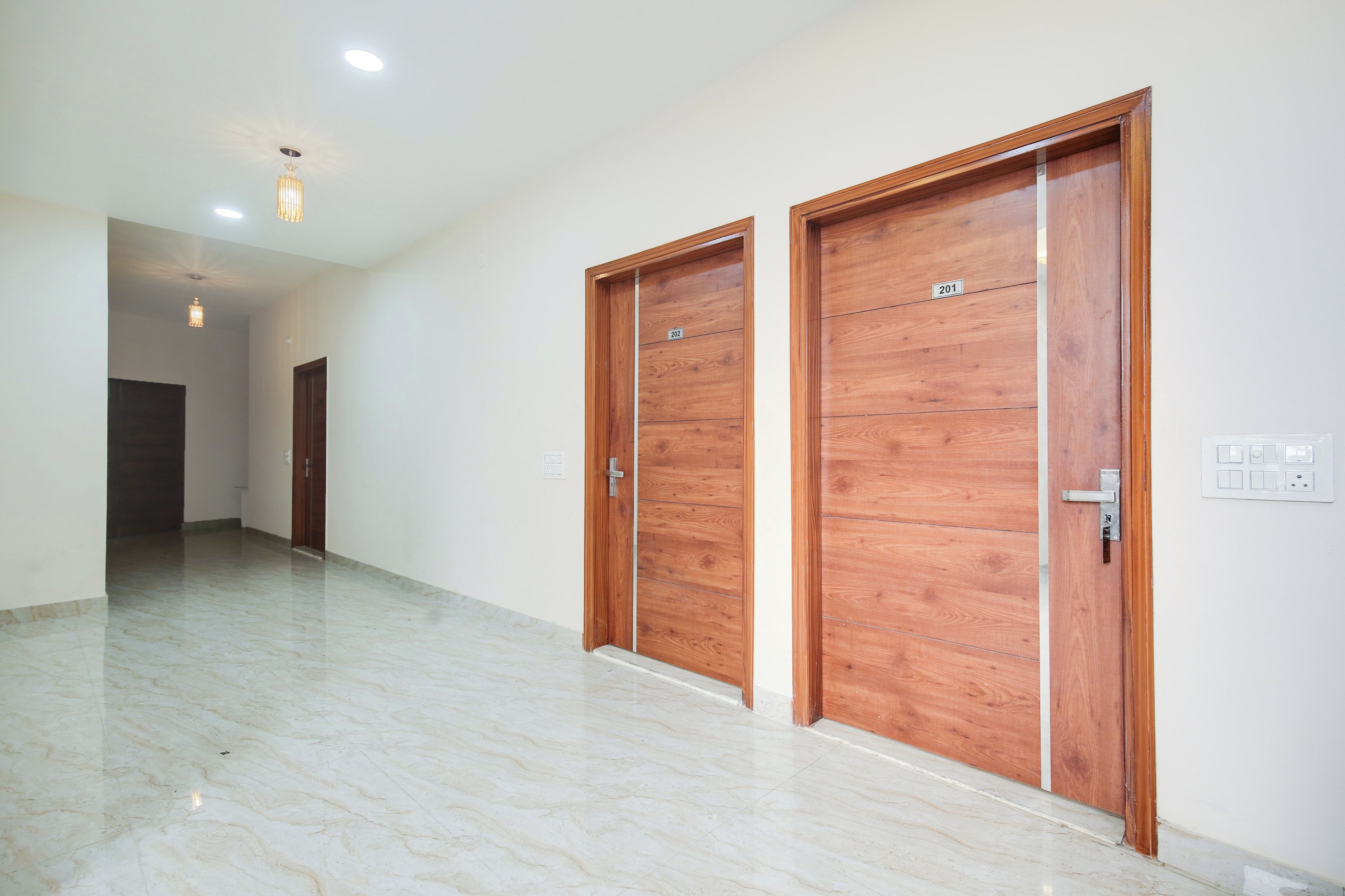 A corridor with two wooden doors, a marble floor, and a ceiling light fixture.