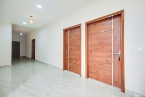 Un pasillo con dos puertas de madera, suelo de mármol y una lámpara en el techo.