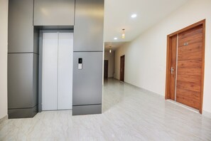 Un pasillo con un ascensor moderno, una puerta de madera y un piso de mármol.