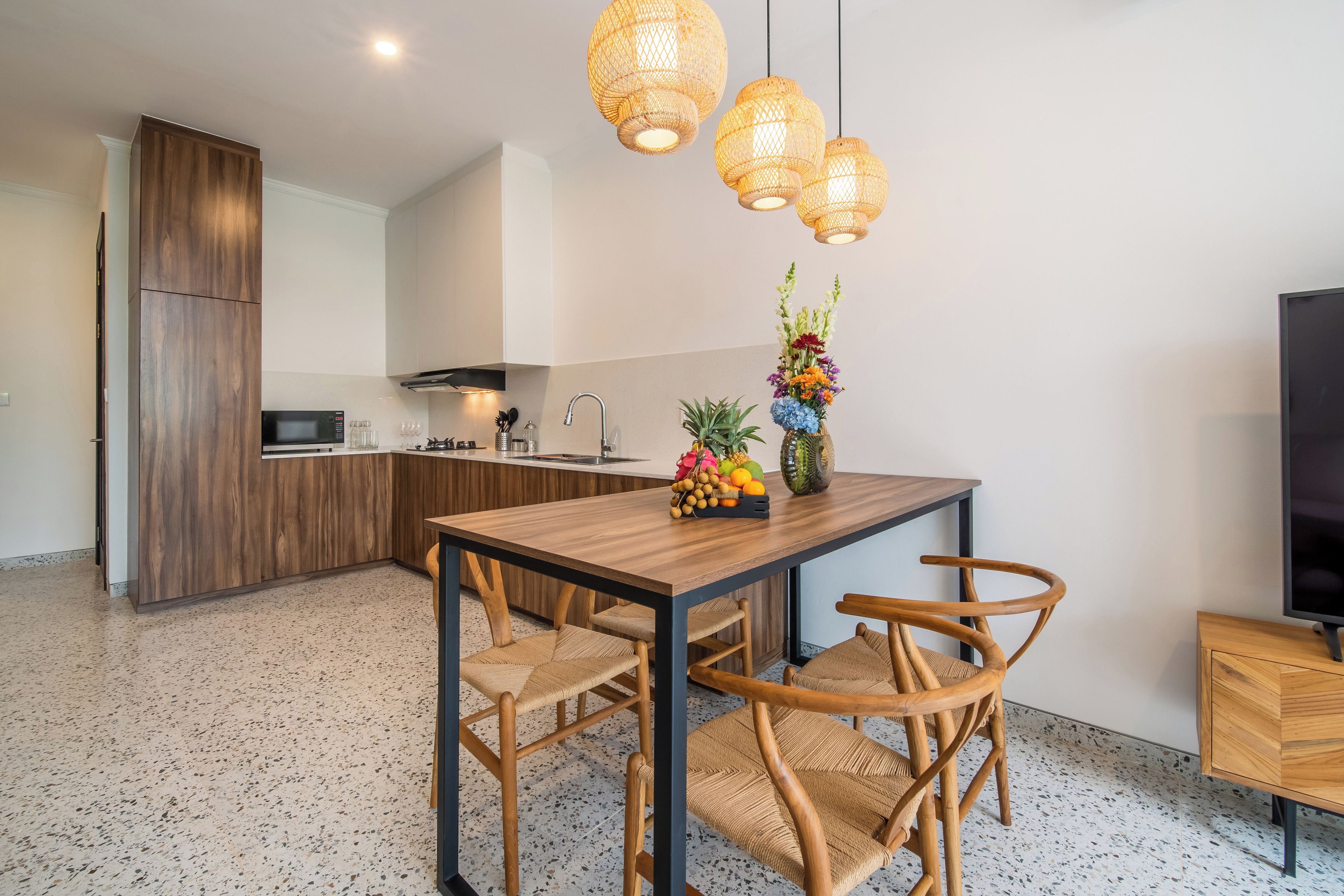 Una cocina moderna con zona de comedor, armarios de madera, microondas integrado y un frutero sobre la mesa.