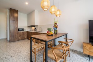 Una cocina moderna con zona de comedor, armarios de madera, microondas integrado y un frutero sobre la mesa.