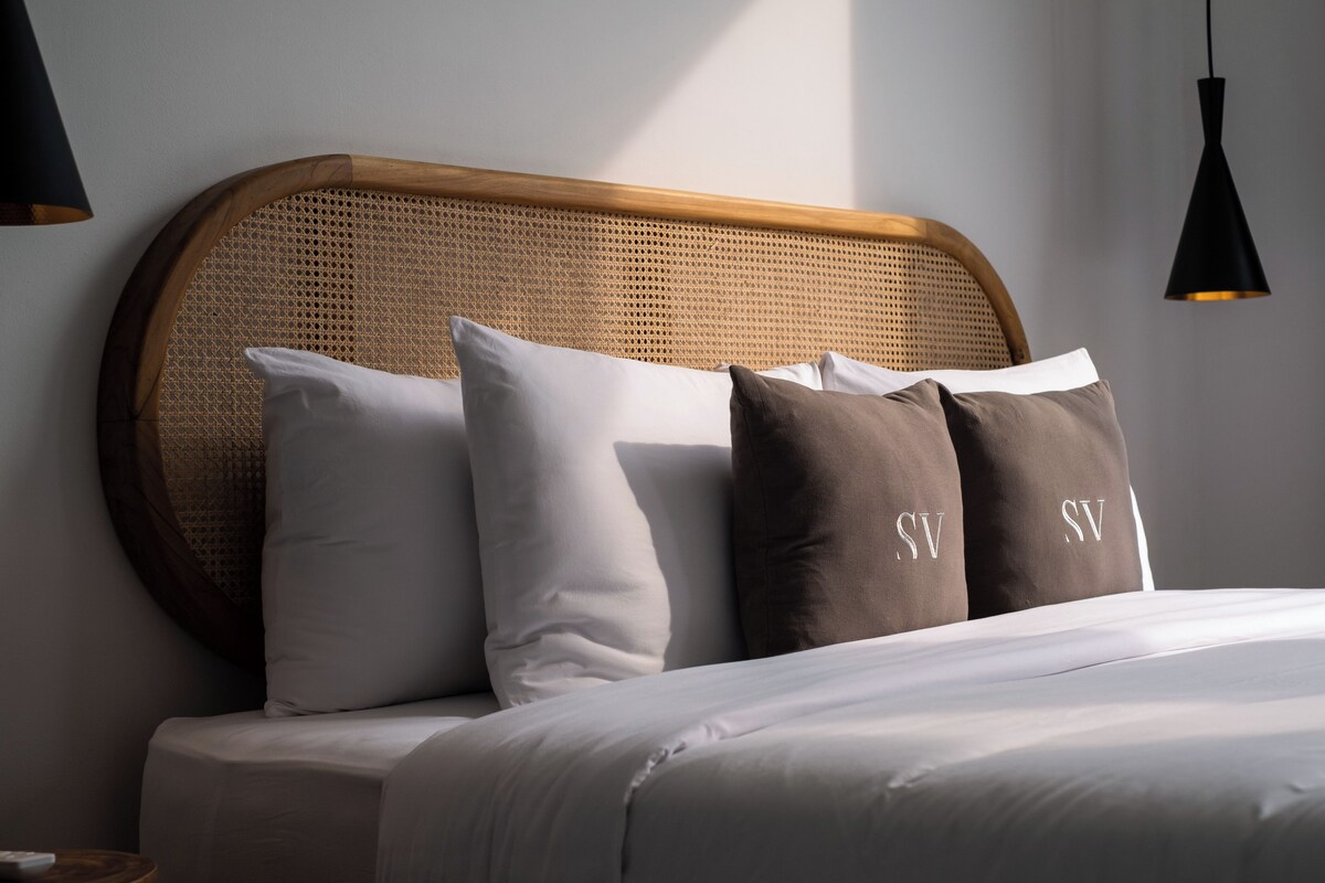 Una cama con cabecera, almohadas y una mesita de noche.