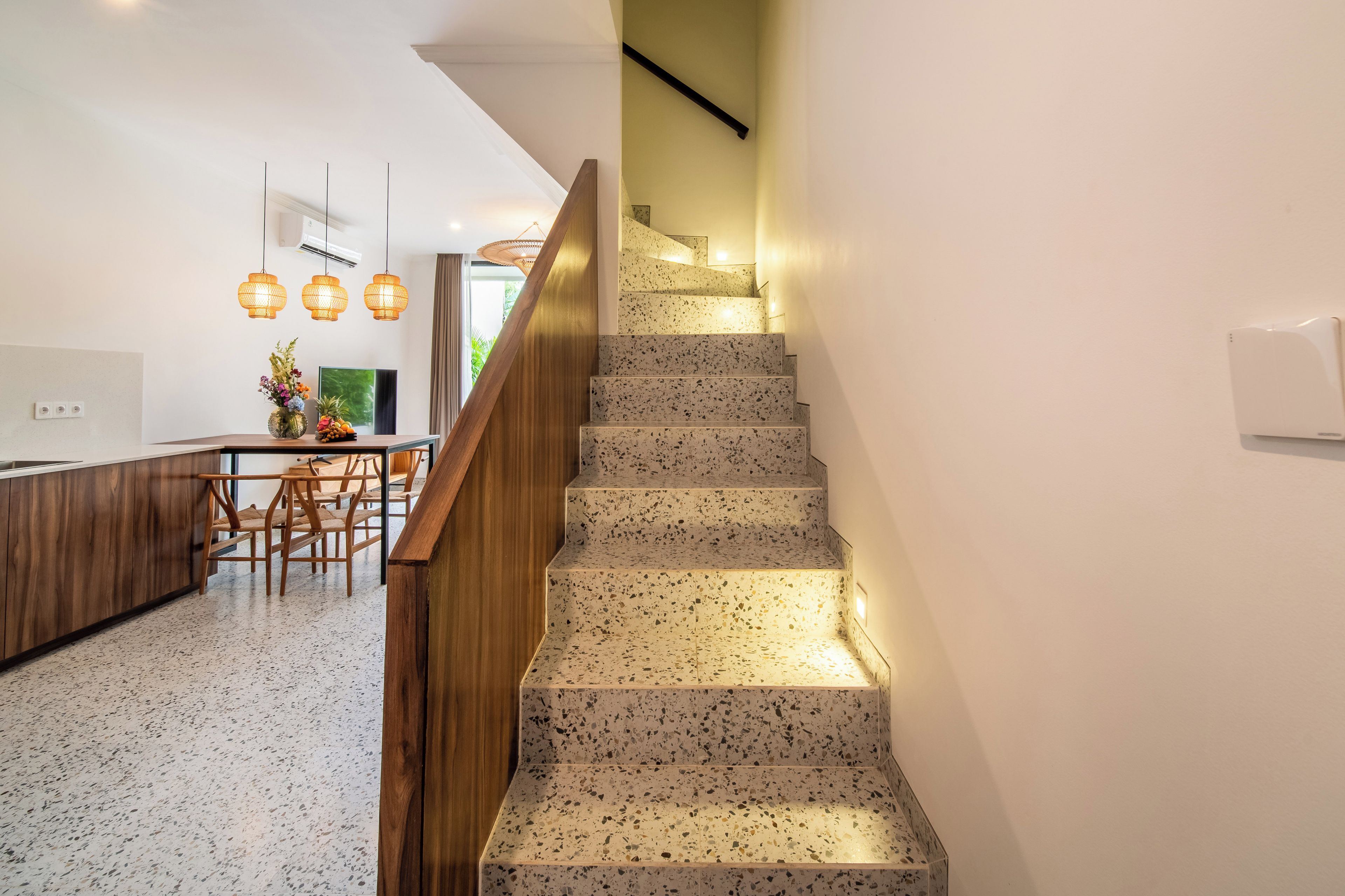Una cocina moderna con comedor, una escalera con barandilla de madera e iluminación colgante.