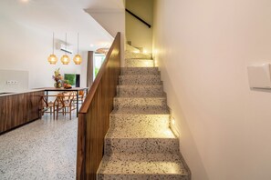 Una cocina moderna con comedor, una escalera con barandilla de madera e iluminación colgante.